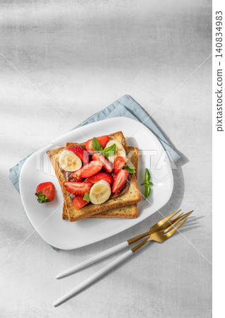 Toasted bread with chocolate cream, strawberries, and banana on a plate on a concrete background Toasted bread with chocolate cream, strawberries, and banana on a plate on a concrete background 140834983