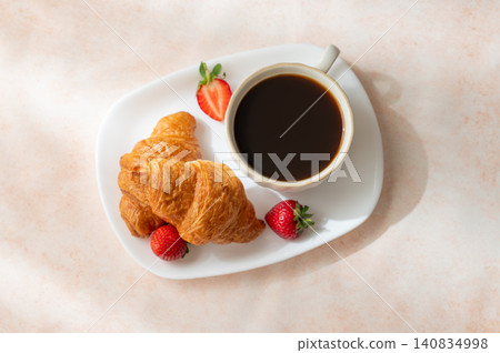 Freshly baked croissants on a plate, cup of espresso coffee and strawberries on a bright background 140834998