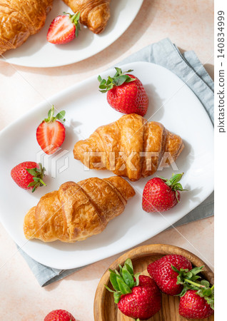 Freshly baked croissants on a plate with strawberries on a bright textured background. Freshly baked croissants on a plate with strawberries on a bright textured background. 140834999