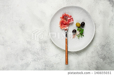 prosciutto on a fork, top view, olives and micro-greens on a plate, light background, no people, prosciutto on a fork, top view, olives and micro-greens on a plate, light background, no people, 140835031