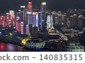 Skyscrapers rise majestically, illuminated by neon blues, vivid crimsons, and stark whites. Vertical light bands mimic glowing waterfalls, while geometric frameworks trace silhouettes against the 140835315