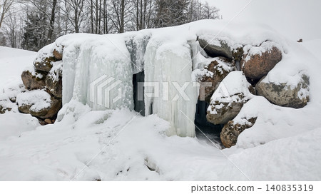A frozen waterfall cascading over large rocks in a snowy winter landscape. 140835319
