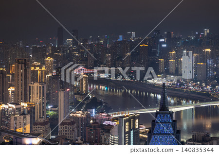 At night, Chongqing unfolds as a dense vertical metropolis of gold and shadow.  countless high-rises stack tightly across the cityscape, their windows glittering with warm golden light. Two distinct 140835344