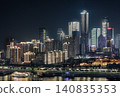 Chongqing nocturnal cityscape unfolds as a towering amphitheater of light. Modern skyscrapers pierce the dark sky with crisp white, amber, and cool aquamarine tones. Layered high-rises stack densely 140835353