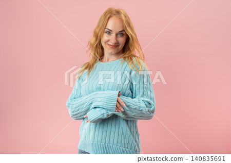 Young woman with red hair wearing a blue knitted sweater, standing confidently against a pink background, showcasing a shy yet warm expression Young woman with red hair wearing a blue knitted sweater, standing confidently against a pink background, showcasing a shy yet warm expression 140835691