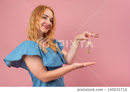 Young woman smiling, presenting a shiny golden house key, symbolizing new home ownership, unlocking opportunities, security, and investing in real estate on a pink background Young woman smiling, presenting a shiny golden house key, symbolizing new home ownership, unlocking opportunities, security, and investing in real estate on a pink background 140835718