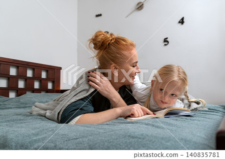 Mother and daughter bonding over a story book while relaxing on the bed, sharing a precious moment of connection and learning in a cozy home environment Mother and daughter bonding over a story book while relaxing on the bed, sharing a precious moment of connection and learning in a cozy home environment 140835781
