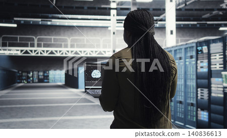 Data center engineer uses laptop in a server room to monitor AI diagnostics and neural network performance. Data center engineer uses laptop in a server room to monitor AI diagnostics and neural network performance. 140836613