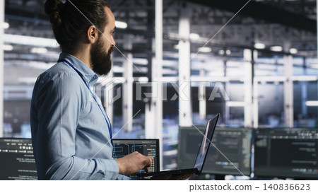 Data center administrator monitors operational metrics on digital device inside a server room to improve infrastructure performance. Data center administrator monitors operational metrics on digital device inside a server room to improve infrastructure performance. 140836623