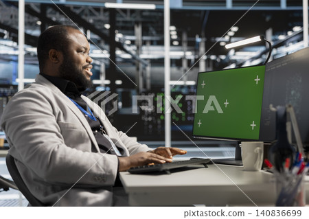IT expert uses a green screen computer in a data center for server operations, screen replacement, and server workflow monitoring. 140836699