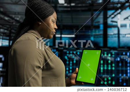 Team supervisor uses a green screen tablet in a data center for hardware diagnostics, screen replacement, and server workflow monitoring. Team supervisor uses a green screen tablet in a data center for hardware diagnostics, screen replacement, and server workflow monitoring. 140836712