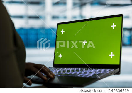 Software developer uses a green screen laptop in a data center for hardware diagnostics, screen replacement, and server workflow monitoring. 140836719