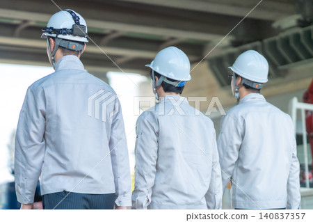 The backs of three male staff members in work clothes heading to a construction site. The backs of three male staff members in work clothes heading to a construction site. 140837357