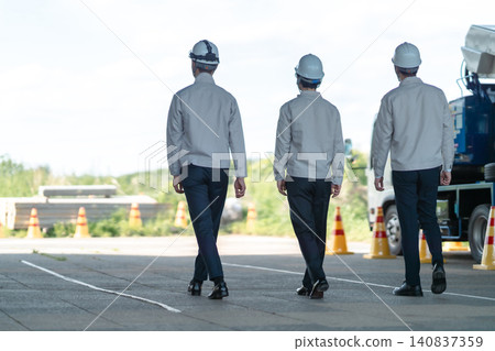 The backs of three male staff members in work clothes heading to a construction site. The backs of three male staff members in work clothes heading to a construction site. 140837359