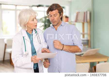 Sad man patient with documents discuss treatment with senior female doctor Sad man patient with documents discuss treatment with senior female doctor 140837706