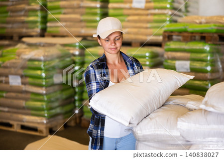 Woman working in warehouse, lifting heavy bag Woman working in warehouse, lifting heavy bag 140838027