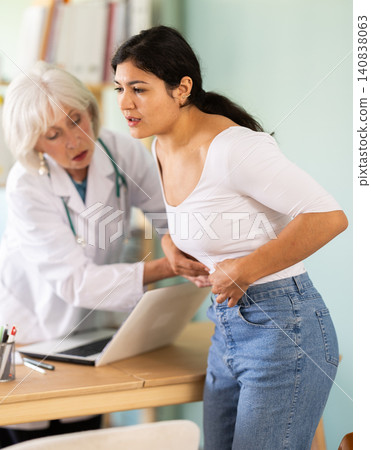 Latin woman holds sore spot one stomach at doctors appointment 140838063