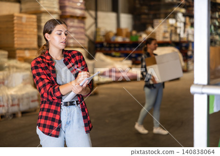 Attentive female manager keeps records of bulk construction materials in warehouse, writing down the data on paper Attentive female manager keeps records of bulk construction materials in warehouse, writing down the data on paper 140838064