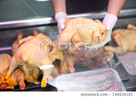 Close-up of sellers hands add put butchered chicken carcass in glass showcase refrigerator. 140838185