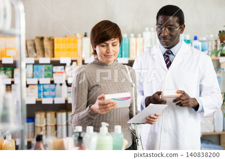 Woman choose buy painkiller tablet at pharmacy. African man in background 140838200