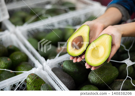 Fresh ripe sliced avocado on hand, blurred boxes with fruits Fresh ripe sliced avocado on hand, blurred boxes with fruits 140838206