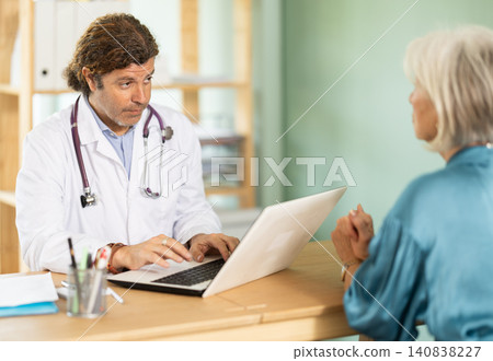 At clinic, senior woman is at doctors appointment, talking at table At clinic, senior woman is at doctors appointment, talking at table 140838227