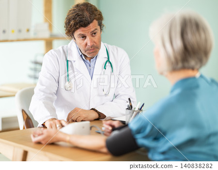 Man doctor measures senior female patients blood pressure at clinic Man doctor measures senior female patients blood pressure at clinic 140838282