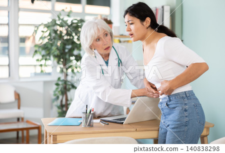 Latin woman holds sore spot one stomach at doctors appointment Latin woman holds sore spot one stomach at doctors appointment 140838298