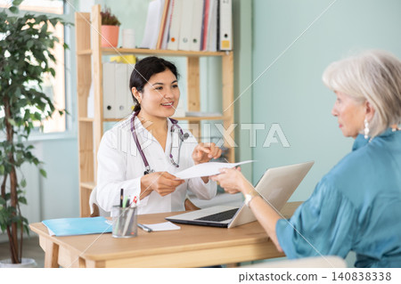At clinic, senior woman is at doctors appointment, talking at table At clinic, senior woman is at doctors appointment, talking at table 140838338