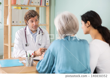 Adult male doctor consulting with adult and elderly women in medical office 140838352