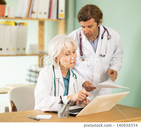 Senior woman and male doctors bent over laptop, work with medical soft Senior woman and male doctors bent over laptop, work with medical soft 140838354
