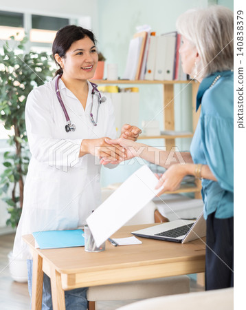Female doctor shaking hands with elderly woman patient at table Female doctor shaking hands with elderly woman patient at table 140838379