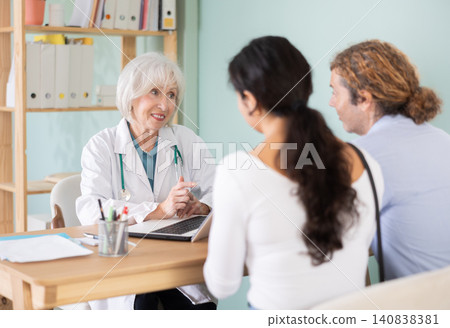 Elderly doctor talking with happy couple at table in medical office Elderly doctor talking with happy couple at table in medical office 140838381