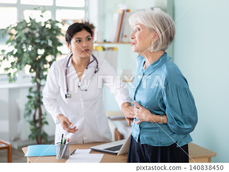 Senior woman holds sore spot one stomach at doctors appointment Senior woman holds sore spot one stomach at doctors appointment 140838450