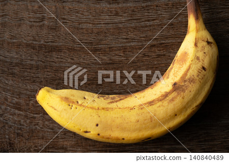 A slightly browned banana against a wood grain background. A slightly browned banana against a wood grain background. 140840489