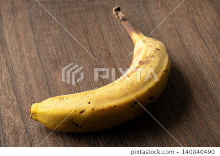 A slightly browned banana against a wood grain background. A slightly browned banana against a wood grain background. 140840490