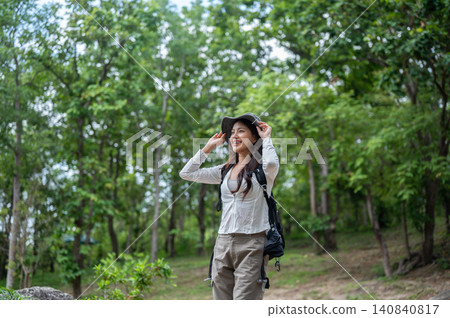 Asian female hiker smiling and adjusting a hat while exploring a green forest on a mountain trail Asian female hiker smiling and adjusting a hat while exploring a green forest on a mountain trail 140840817