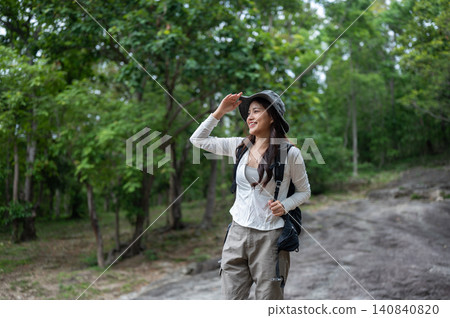 Cheerful asian woman hiker traveler enjoying a scenic forest trail surrounded by lush green nature. Cheerful asian woman hiker traveler enjoying a scenic forest trail surrounded by lush green nature. 140840820
