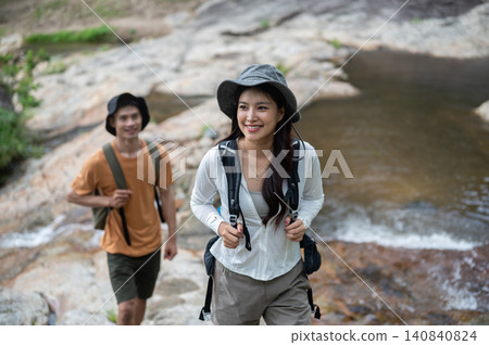 Smiling asian woman tourist walking ahead of man friend on rock in forest on a mountain hiking trail 140840824