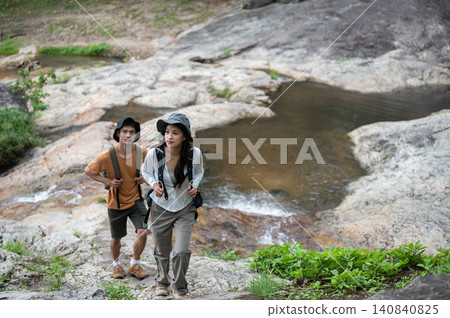 Two hikers asian man and woman climb a rocky trail beside a stream, exploring the wilderness together Two hikers asian man and woman climb a rocky trail beside a stream, exploring the wilderness together 140840825