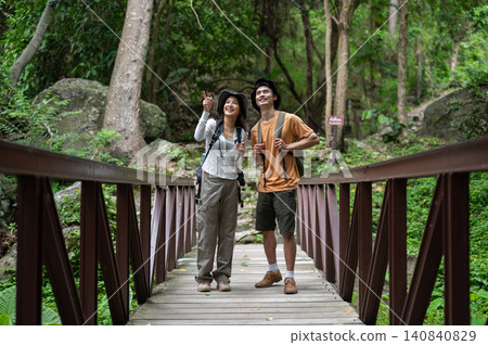 Two hikers asian man and woman pause on a forest bridge, admiring nature during their mountain trail Two hikers asian man and woman pause on a forest bridge, admiring nature during their mountain trail 140840829