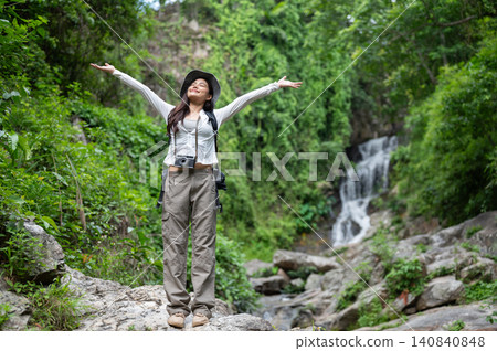 Happy asian woman tourist raising both arms standing on waterfall's rocks in forest on hiking trail. Happy asian woman tourist raising both arms standing on waterfall's rocks in forest on hiking trail. 140840848