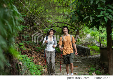 Happy asian male and female hikers walking with staff through lush green forest on a mountain trail Happy asian male and female hikers walking with staff through lush green forest on a mountain trail 140840868