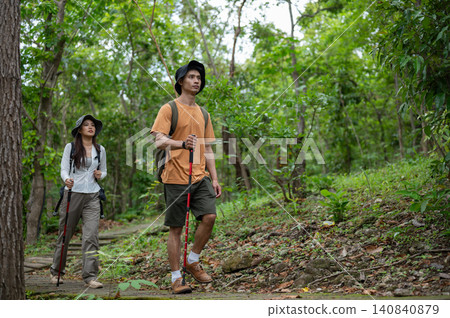 Asian male and female companion hikers explore a path in green tropical forest on a mountain trail Asian male and female companion hikers explore a path in green tropical forest on a mountain trail 140840879