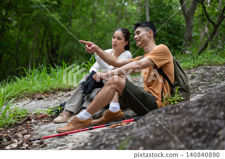 Asian male and female hikers resting, pointing and enjoying forest views together on mountain trail 140840890