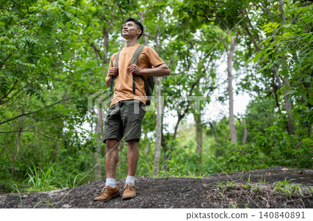 Asian male hiker with backpack enjoying a green forest view over rocky terrain on a mountain trail. Asian male hiker with backpack enjoying a green forest view over rocky terrain on a mountain trail. 140840891