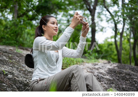 Asian female hiker taking photos with a smartphone while resting in the forest on a mountain trail 140840899
