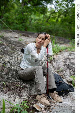 Pretty asian woman tourist holding leaning on trekking staff sitting on ground during a hiking trail 140840900
