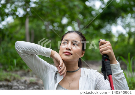 Pretty asian woman tourist holding trekking staff wiping sweat in forest while going on hiking trail 140840901