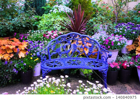 A blue iron bench adorned with roses and a garden of colorful flowers A blue iron bench adorned with roses and a garden of colorful flowers 140840975